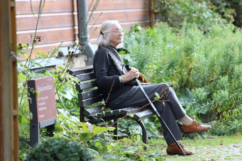 Oudere vrouw met wandelstok zittend op bankje