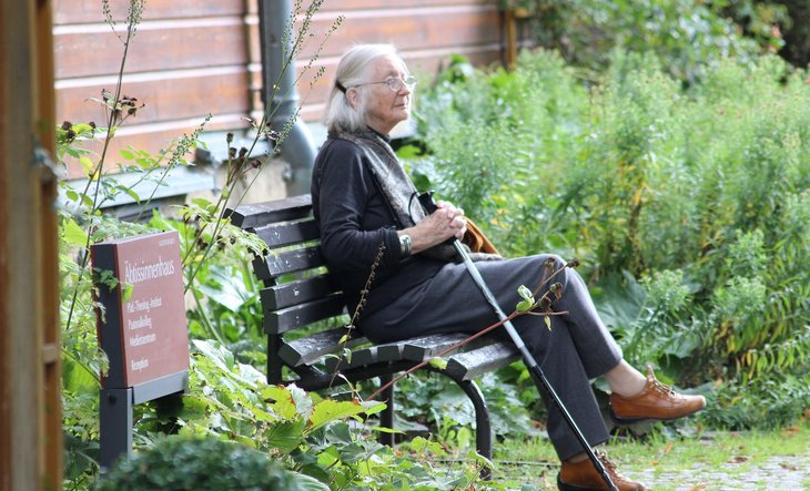 Oudere vrouw met wandelstok zittend op bankje