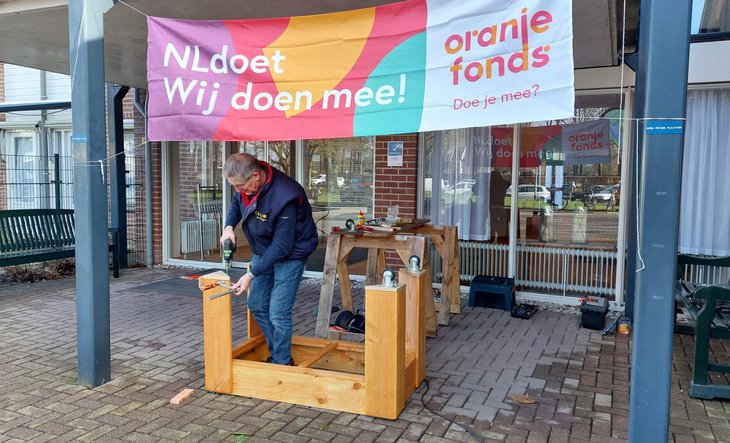 Man aan het klussen onder spandoek van NLdoet