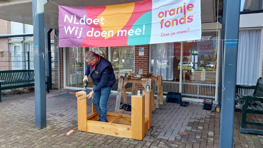 Man aan het klussen onder spandoek van NLdoet