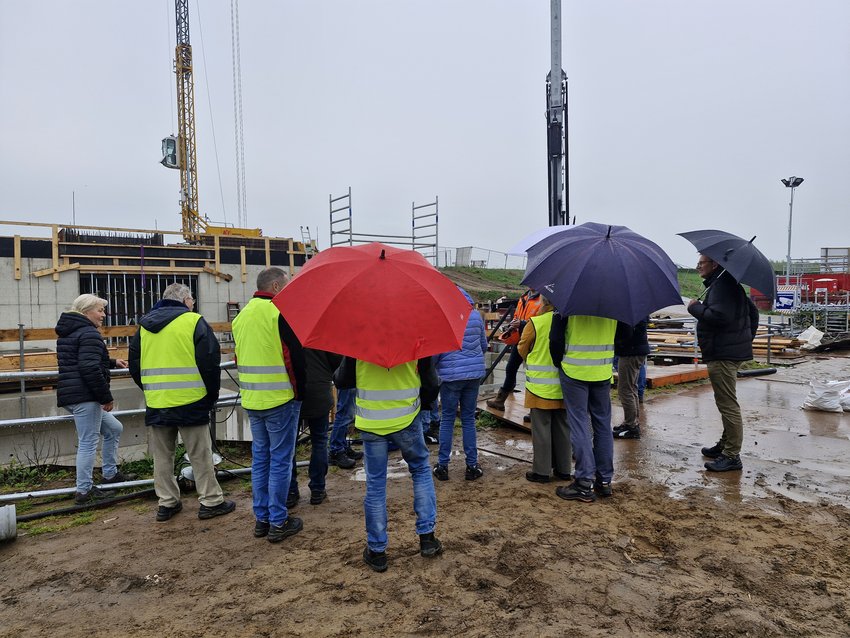 Belangstellenden met paraplu's op de bouwplaats