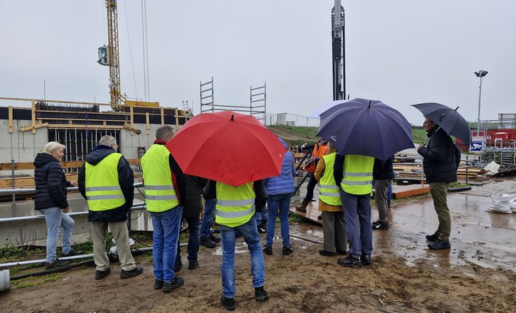 Belangstellenden met paraplu's op de bouwplaats