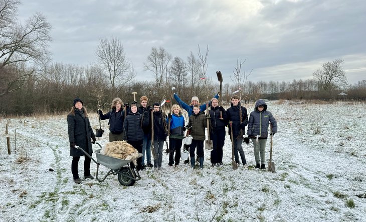 Groep jongeren met docenten buiten om bomen te planten