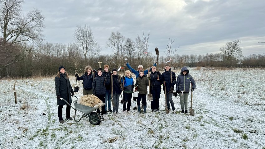 Groep jongeren met docenten buiten om bomen te planten