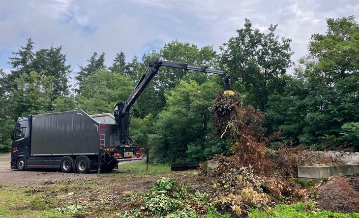 Vrachtwagen met grijparm laadt snoeiafval in